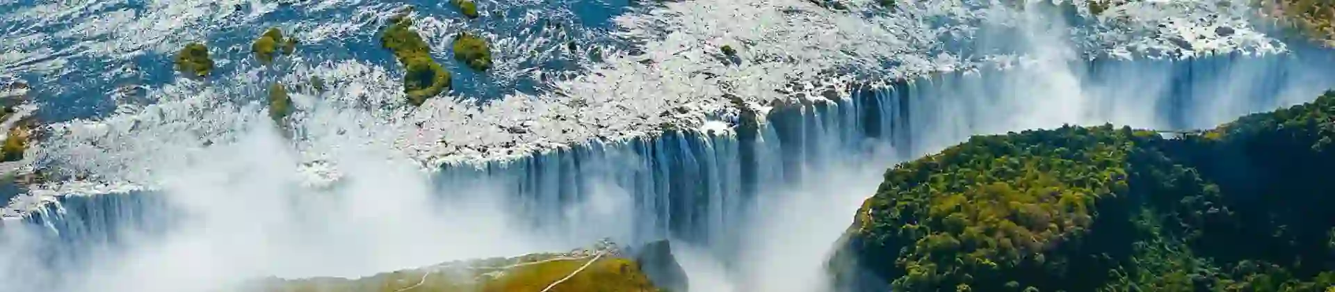 Aerial view of Victoria Falls in Zimbabwe, with water cascading over the cliffs and mist rising above the surrounding landscape