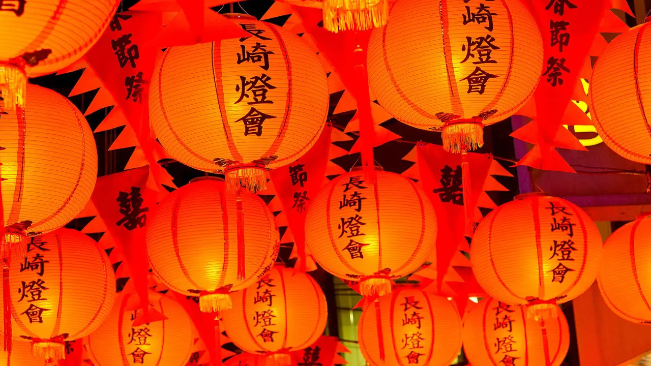 Bright orange-red paper lanterns with Japanese characters hanging overhead during a traditional festival in Kyushu, Japan