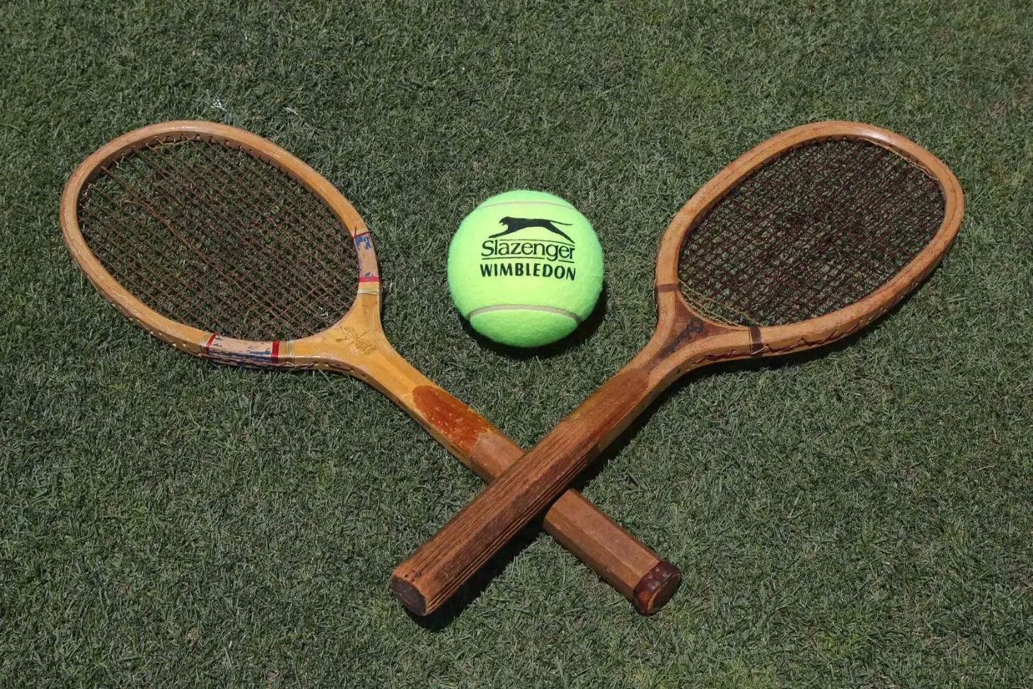 Two wooden tennis rackets and a yellow Slazenger tennis ball arranged on a green lawn