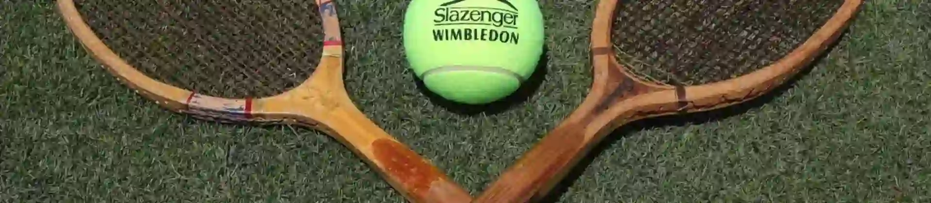 Two wooden tennis rackets and a yellow Slazenger tennis ball arranged on a green lawn