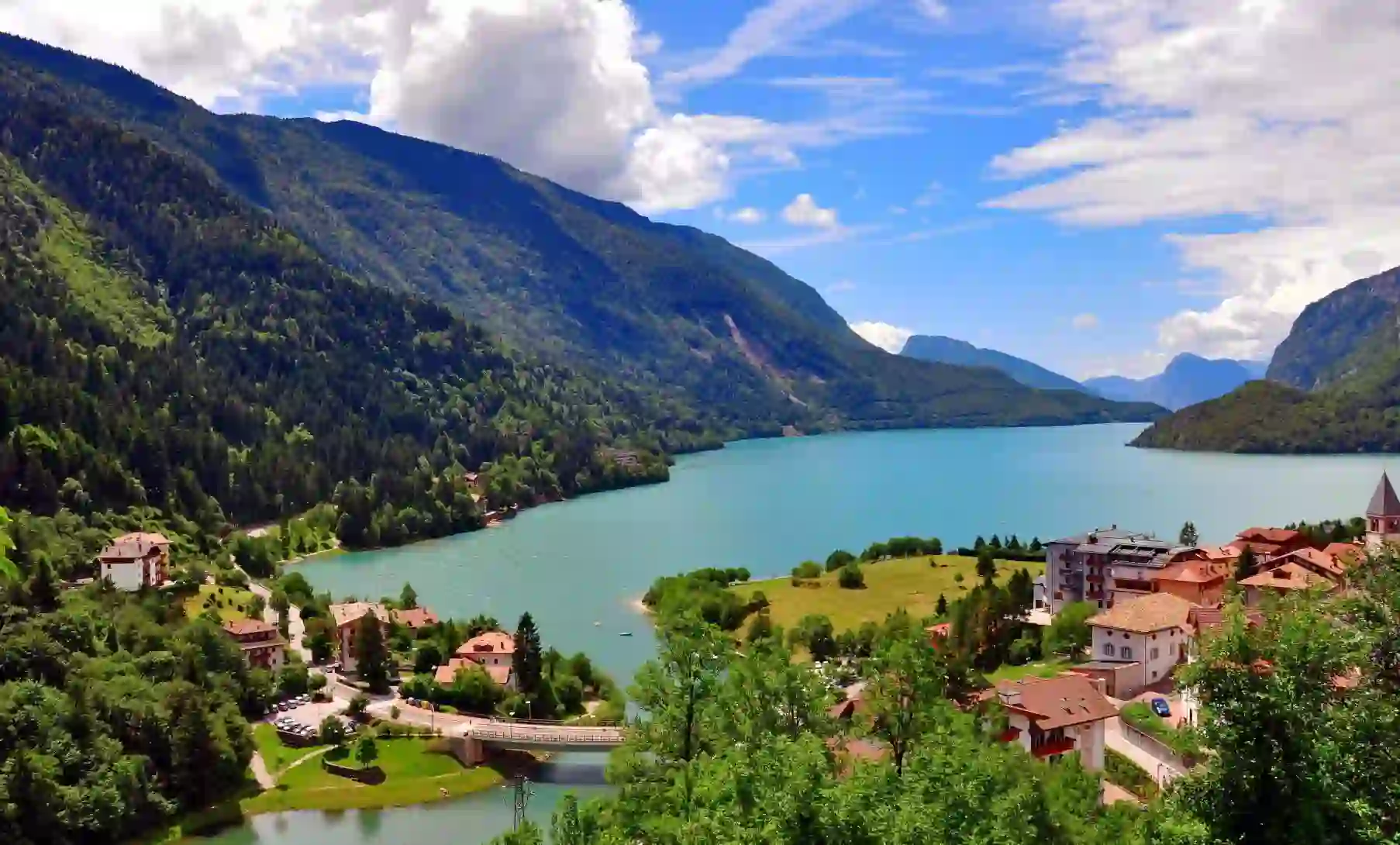 Molveno Lake in Italy, with colourful houses in the foreground and rolling hills alongside the lake