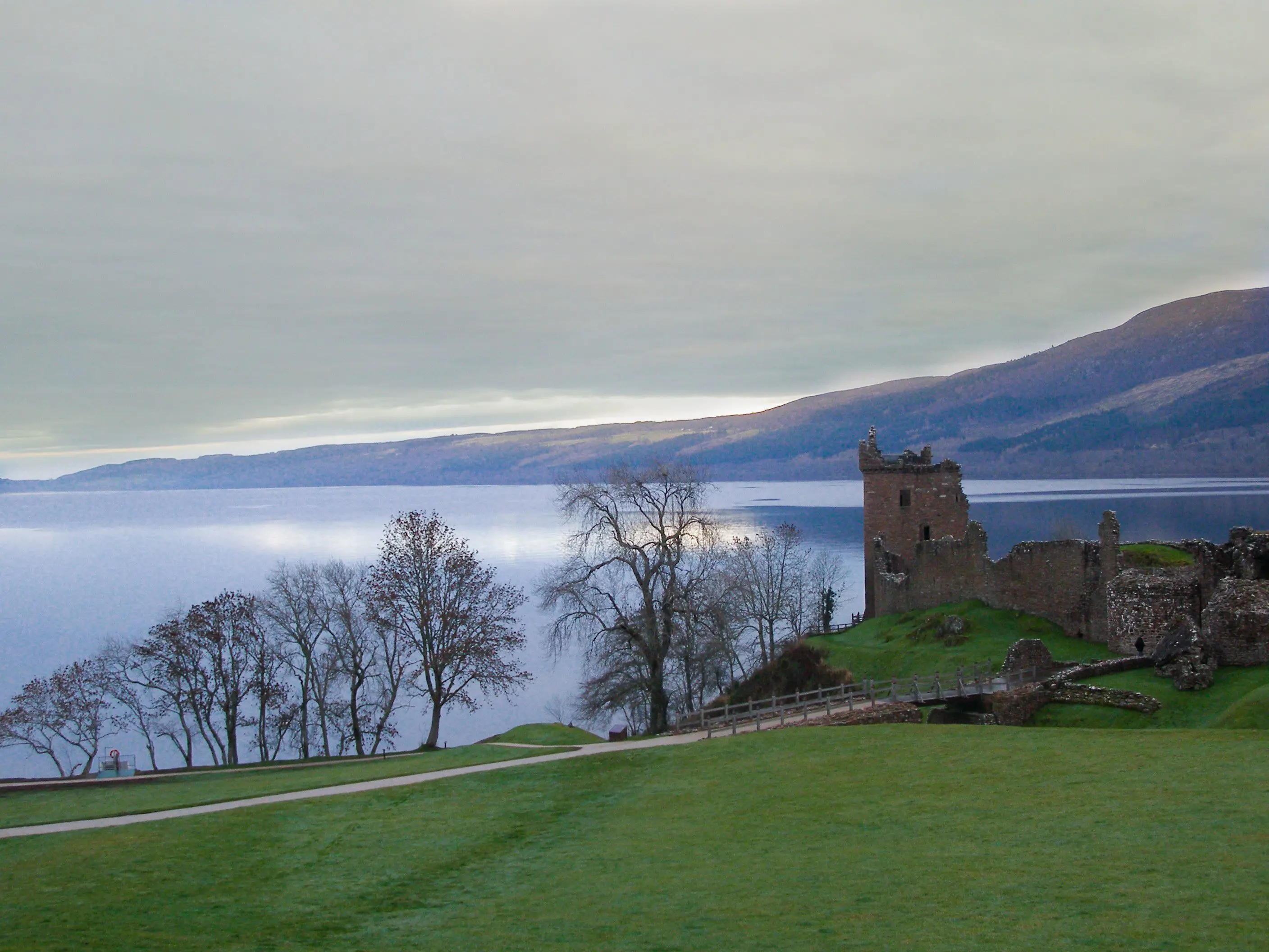 Urquhart Castle overlooking Loch Ness, with grass and leaveless trees in the forefront