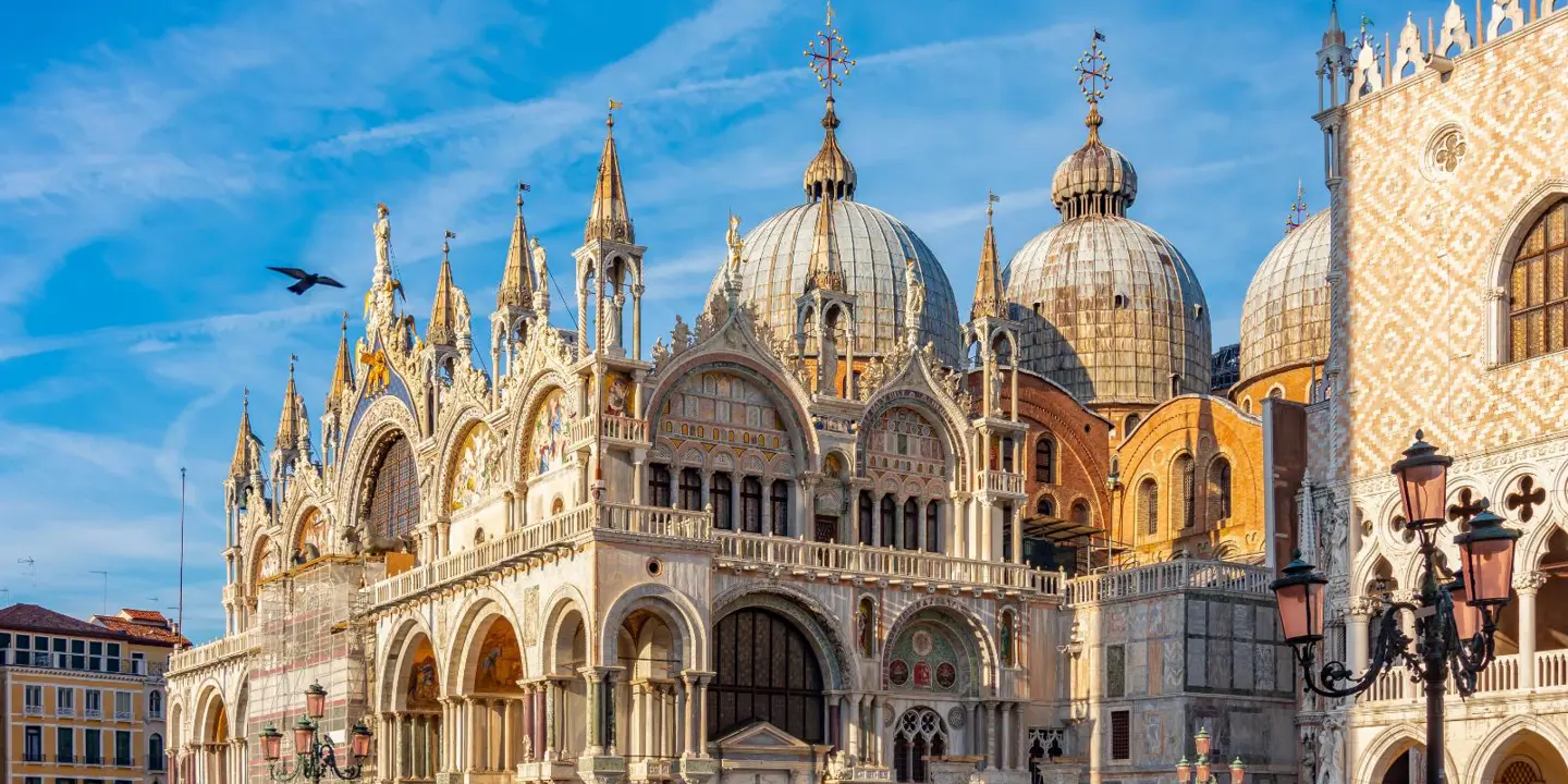 Exterior view of Saint Mark’s Basilica in Venice, Italy, showcasing its ornate façade with domes, arched windows, and detailed mosaics, reflecting Byzantine architectural style