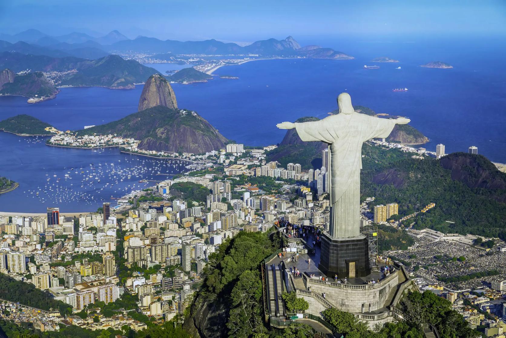 Panoramic view of Rio de Janeiro with Sugarloaf Mountain, the Christ the Redeemer statue, and city buildings along the coastline