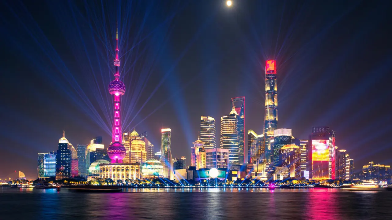 The Oriental Pearl Tower and skyscrapers glowing with colourful laser beams and reflections over the Huangpu River, Shanghai, China