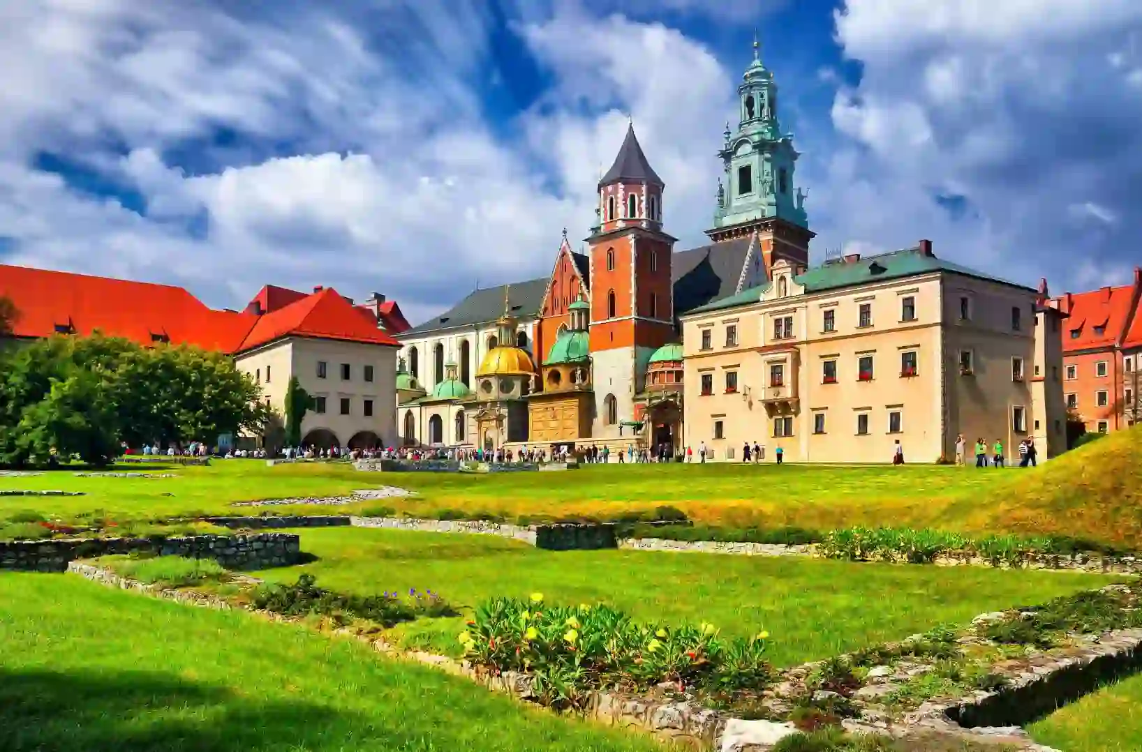 Wawel Castle in Kraków, Poland, showcasing its historic towers and red-brick walls beneath a cloudy blue sky