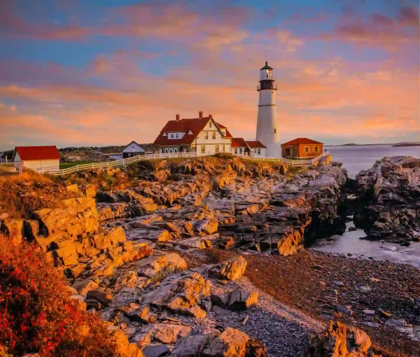 Portland Head Lighthouse on the rocky Maine coast at sunset, with warm colours in the sky reflecting over the Atlantic Ocean