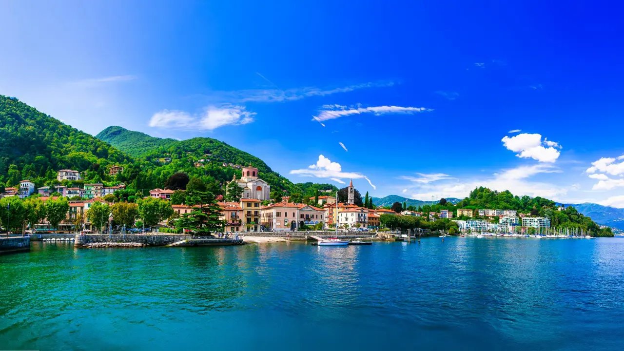 Lake Maggiore in Italy, with an Italian town on the shore beneath a bright, partly cloudy sky