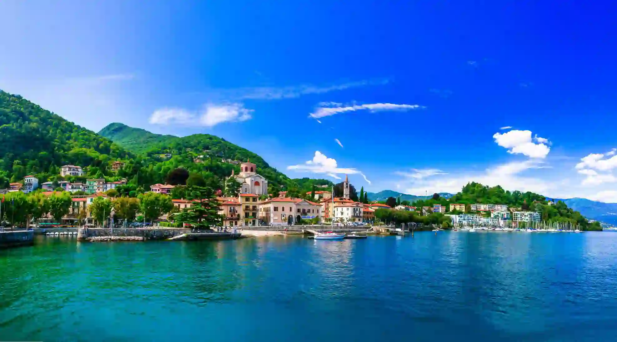 Lake Maggiore in Italy, with an Italian town on the shore beneath a bright, partly cloudy sky