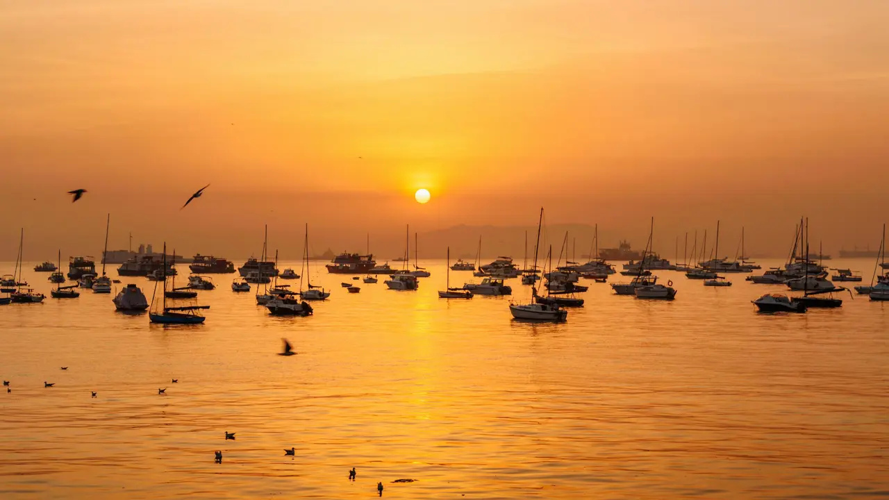Sunset over Mumbai Harbour, with sailboats scattered across the shimmering water