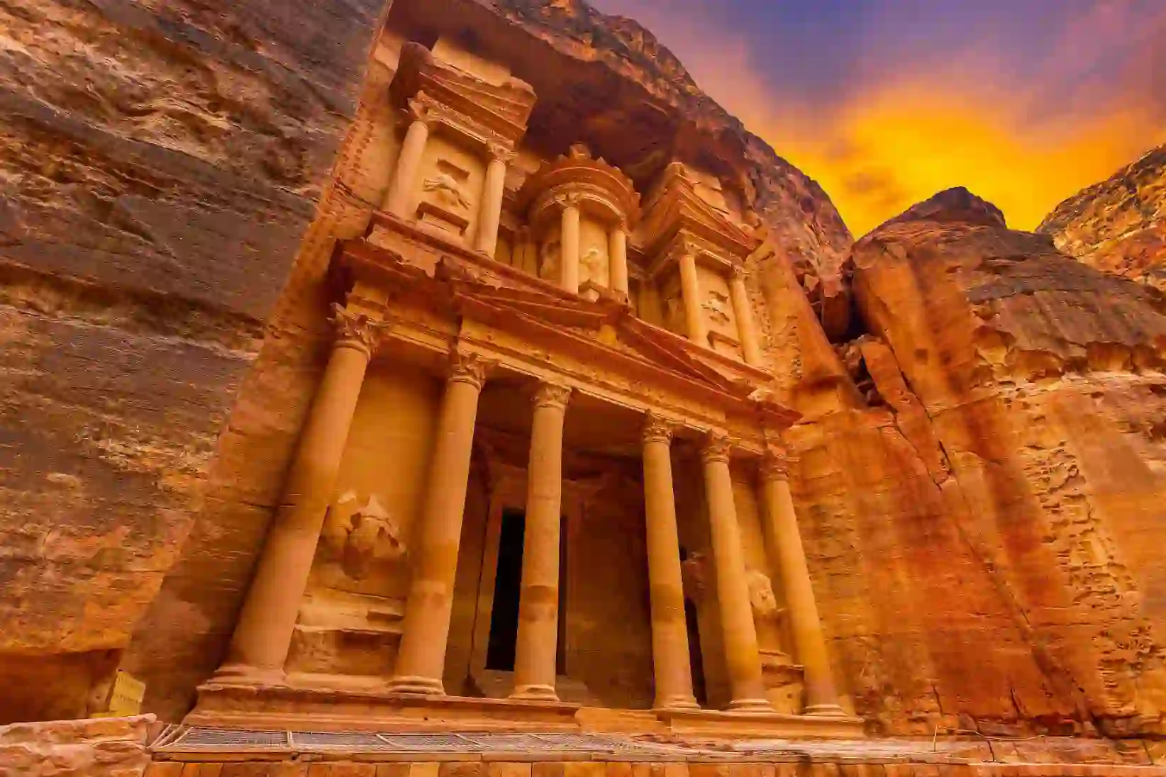 The ancient rock-cut façade of Al-Khazneh, known as the Treasury, at Petra, Jordan, glowing under a vibrant sunset sky