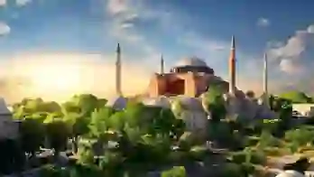 Hagia Sophia with its domes and minarets at sunset, surrounded by green trees in Istanbul
