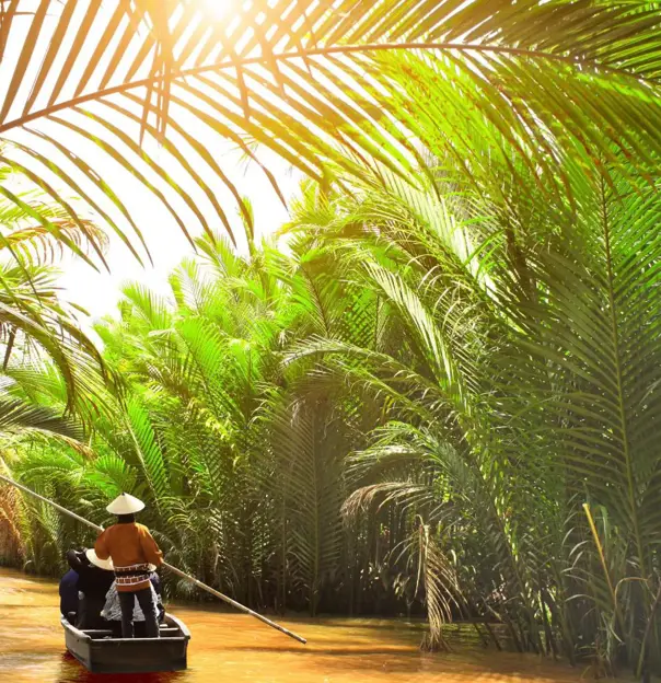 Small wooden boats glide through a palm-lined canal off the Mekong River in Thailand, with a person in a conical hat steering under filtered sunlight