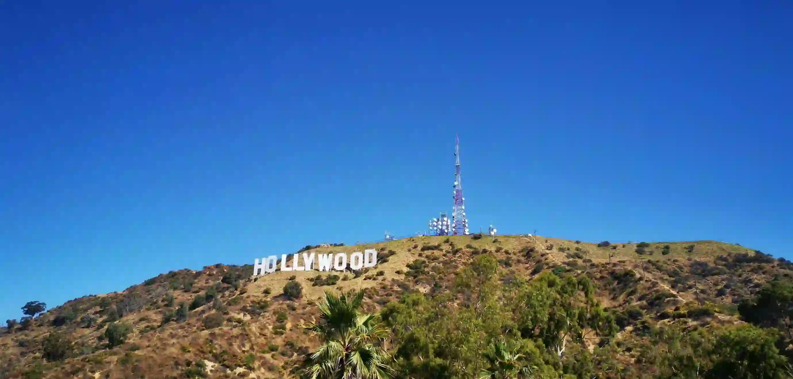 View of the iconic Hollywood sign on a hillside in Los Angeles, with clear blue sky and surrounding greenery