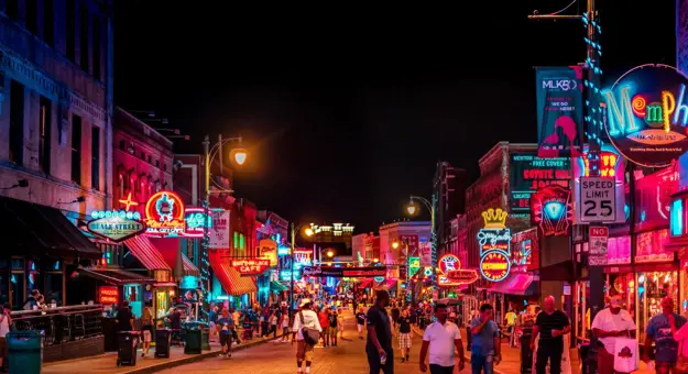 Vibrant night scene on Beale Street in Memphis, with neon signs glowing above blues clubs, bars, and live music venues, and crowds of people walking along the historic street