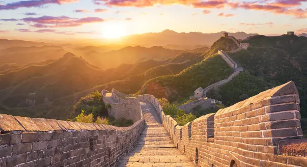 The Great Wall winding over mountain ridges, glowing in golden light at sunset, near Beijing, China