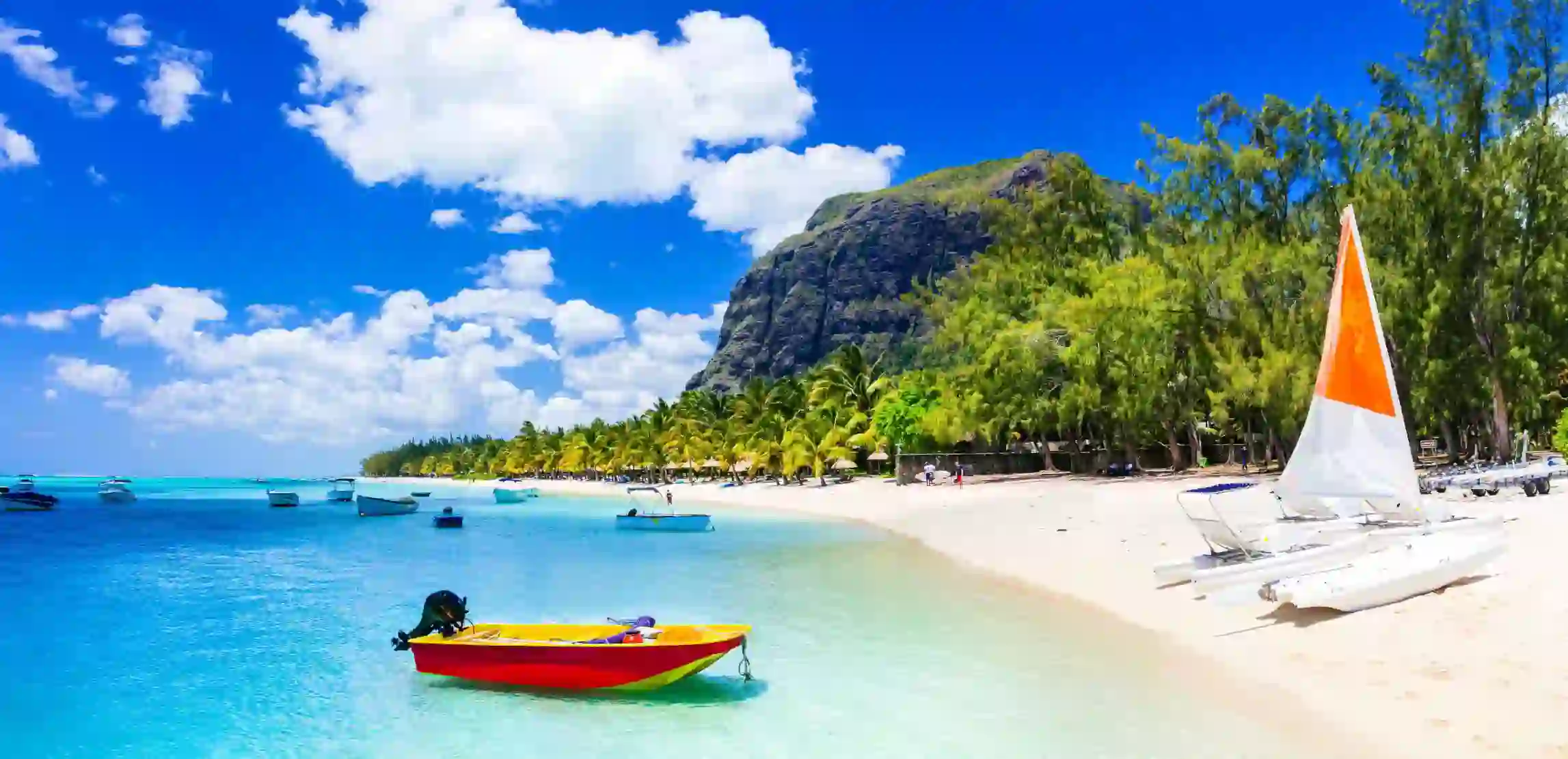 View of Mauritius featuring clear blue water, several boats floating on the sea, and a yacht on the sandy shore