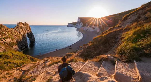 A person sitting on some steps overlooking the beach as the sunsets over the Jurassic Coast, Dorset