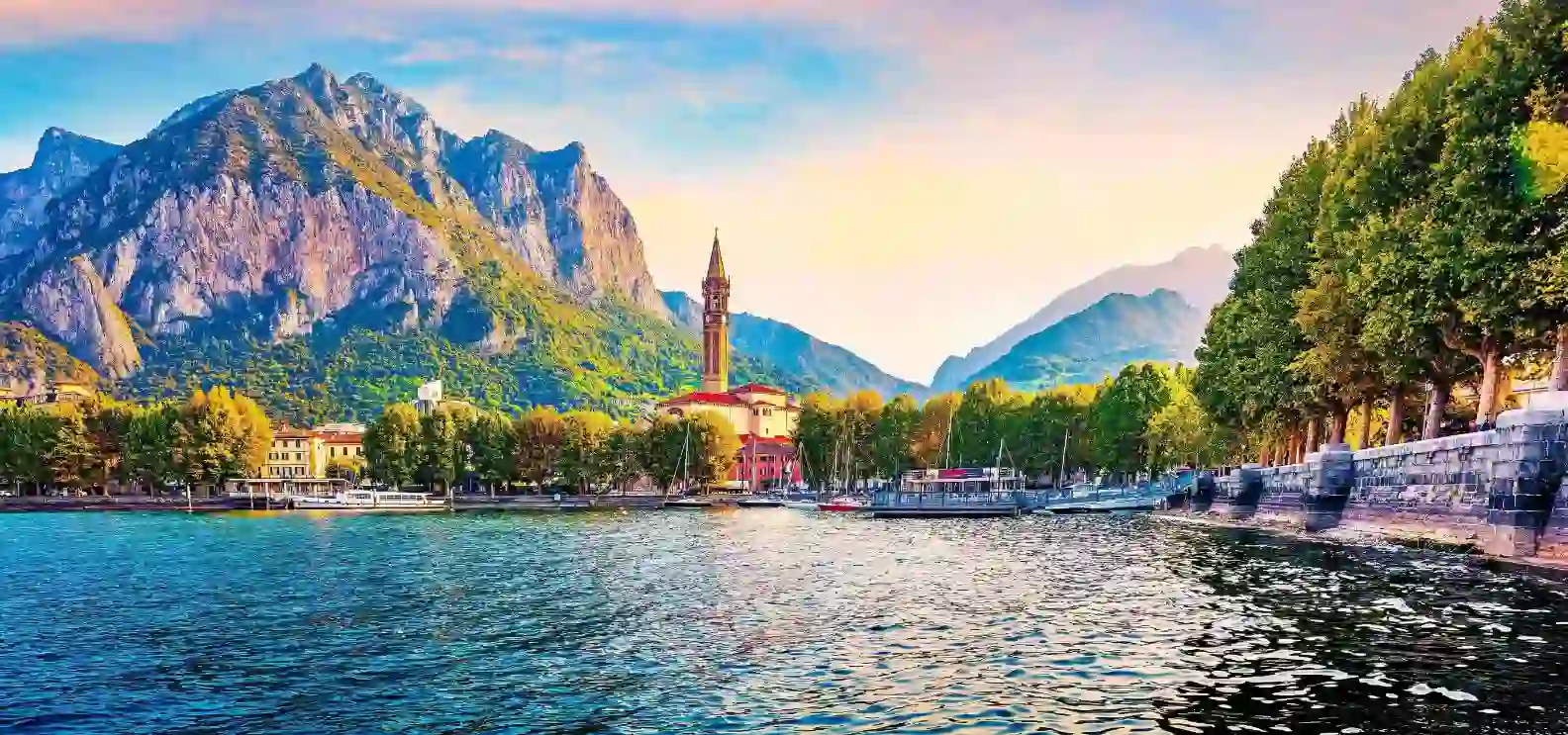 A view of Lake Como with a small church tower and mountains and trees in the background