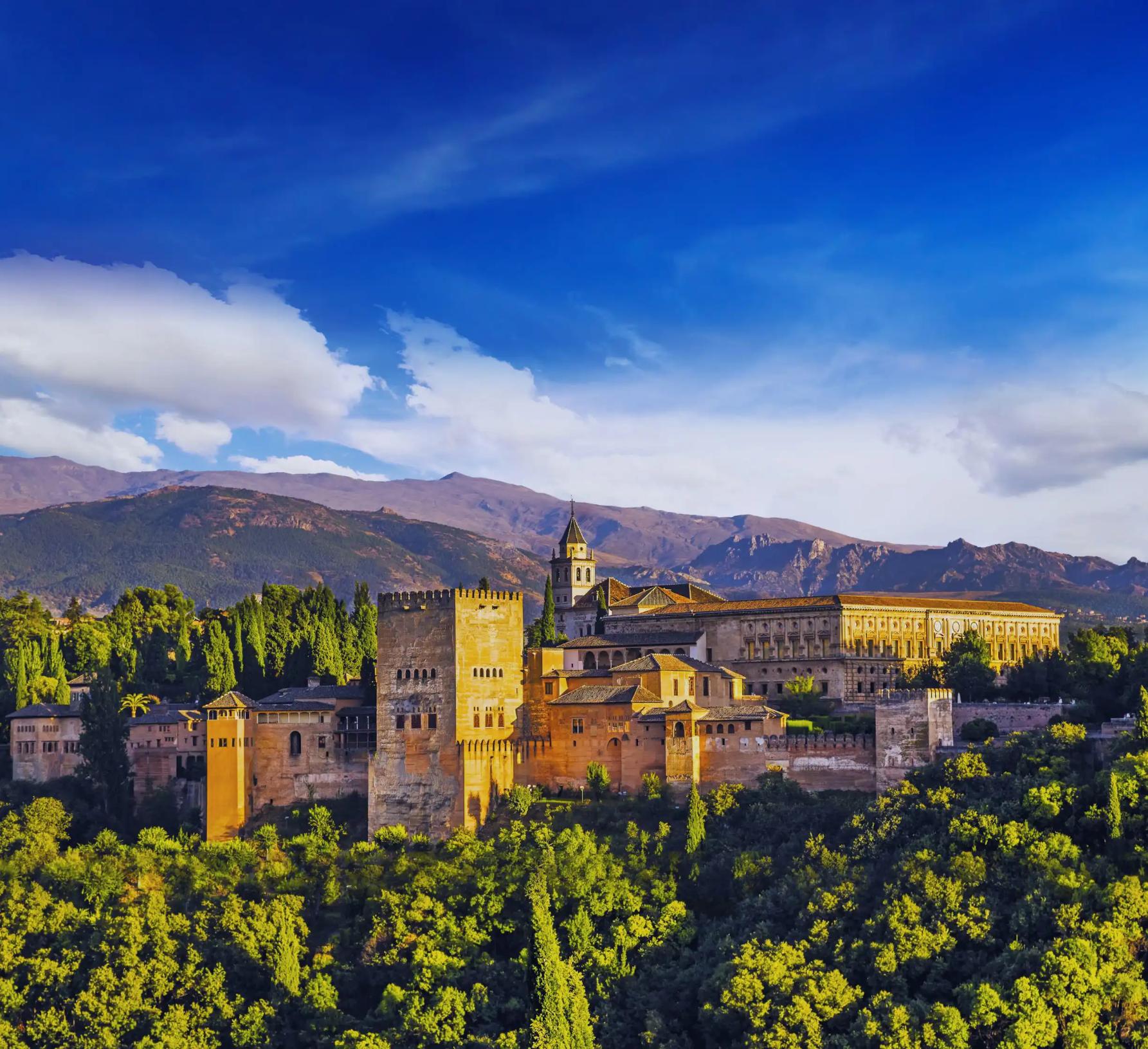Panoramic view of the Alhambra Palace in Spain on a sunny day, with its historic architecture set against a backdrop of rolling hills and a bright blue sky
