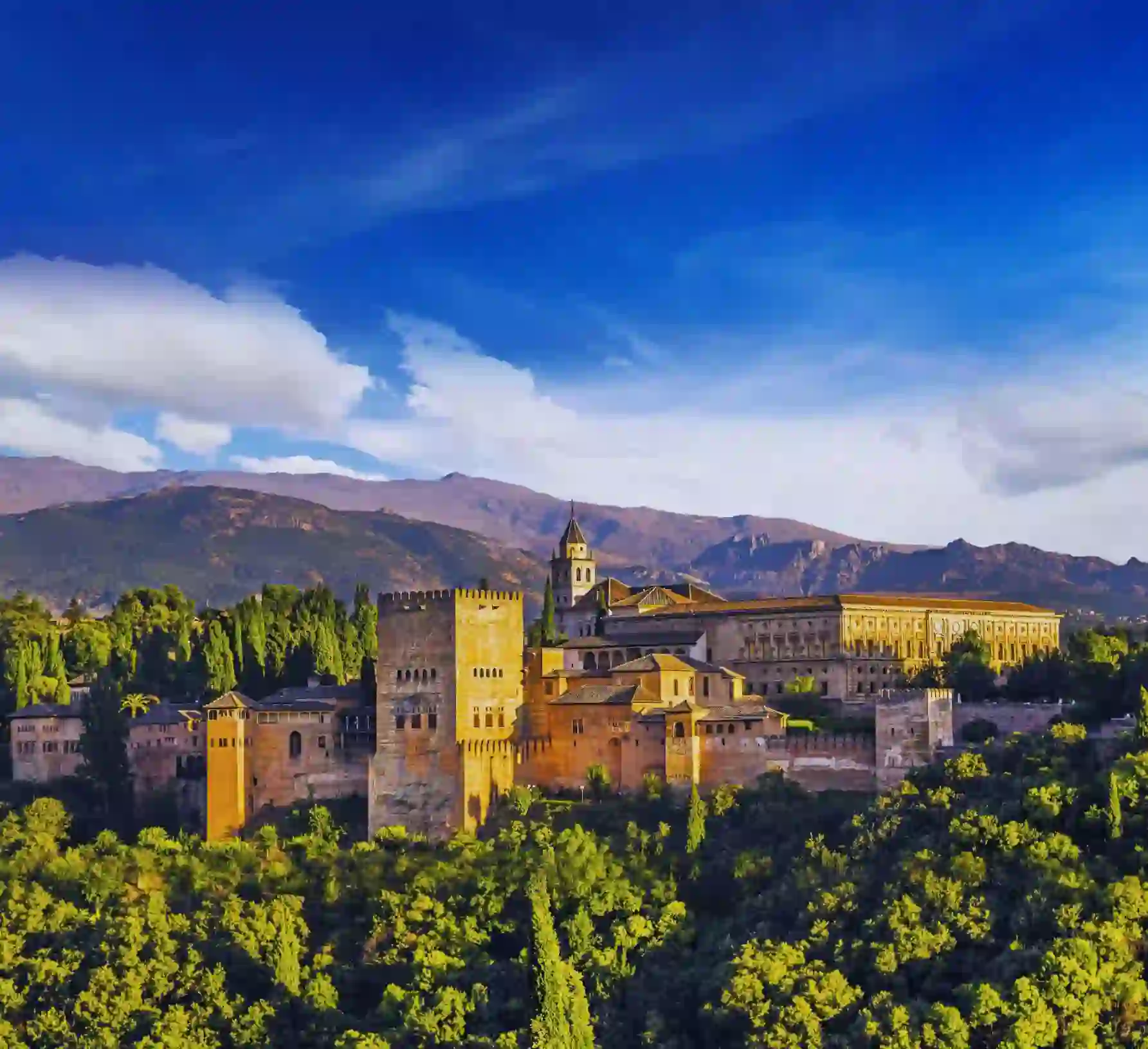 Panoramic view of the Alhambra Palace in Spain on a sunny day, with its historic architecture set against a backdrop of rolling hills and a bright blue sky