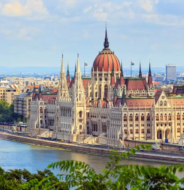 High angle shot of the Hungarian Parliament Building, with red roofs and spiky turrets and the Danube river in the left forefront