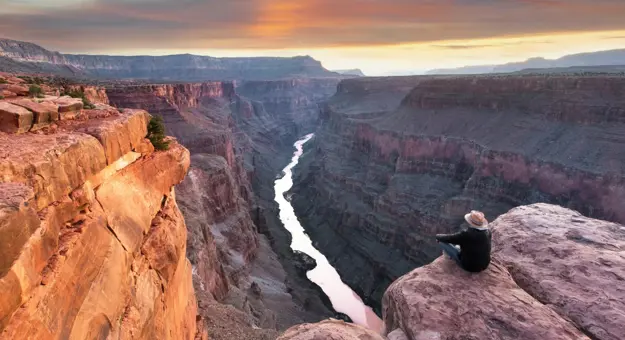 Toroweap Point at the Grand Canyon, with a person sitting near the edge, overlooking the vast canyon landscape as the sun sets