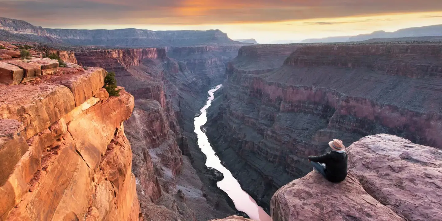 Toroweap Point at the Grand Canyon, with a person sitting near the edge, overlooking the vast canyon landscape as the sun sets