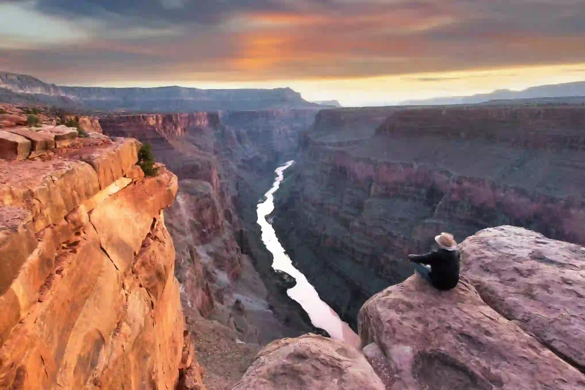 Toroweap Point at the Grand Canyon, with a person sitting near the edge, overlooking the vast canyon landscape as the sun sets