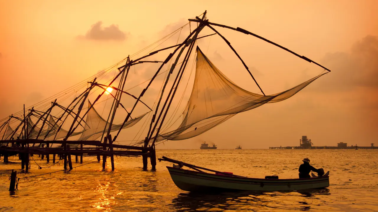 Chinese fishing nets at sunset in Kochi, India, silhouetted against the glowing sky and calm water
