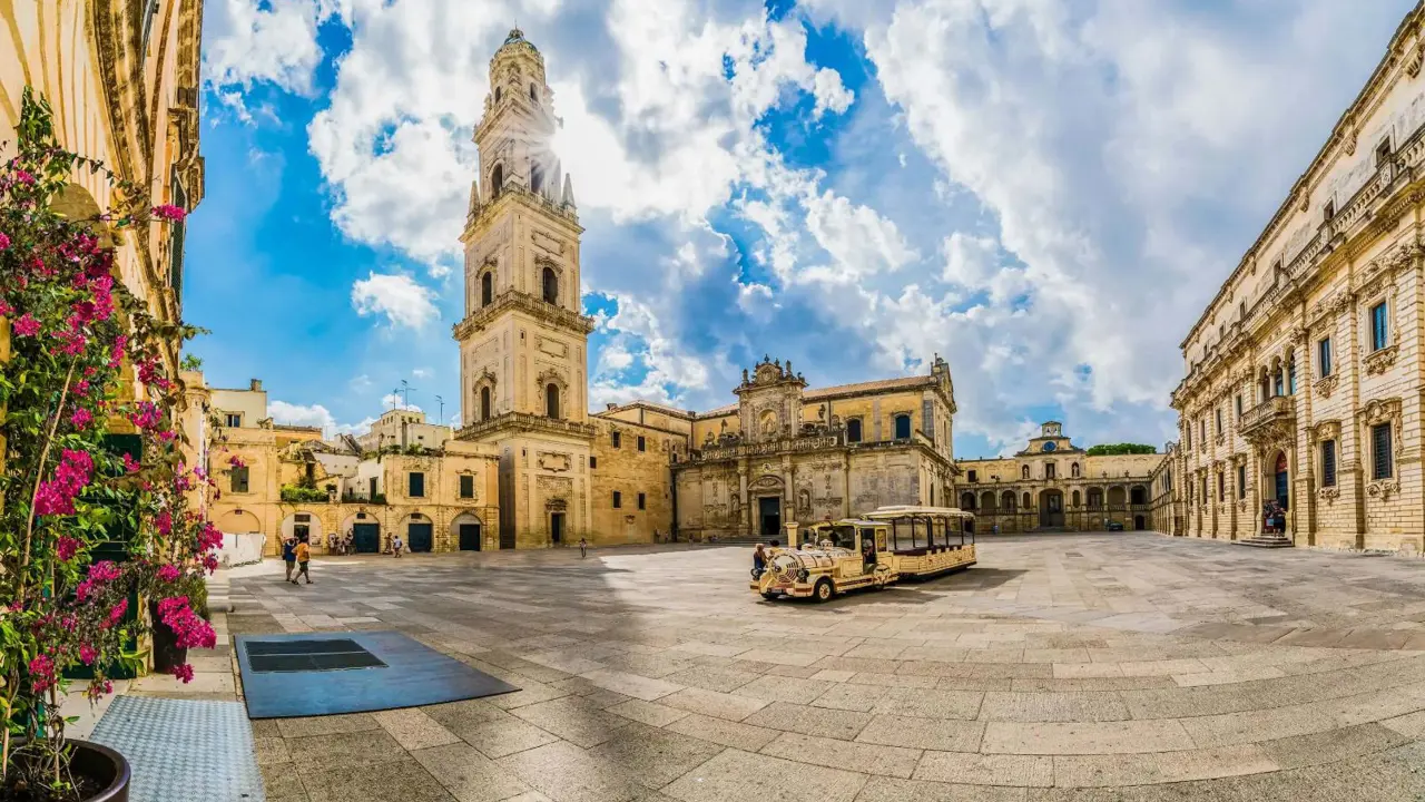 A square in Lecce, Italy, featuring a historic tower and a land train for tourists