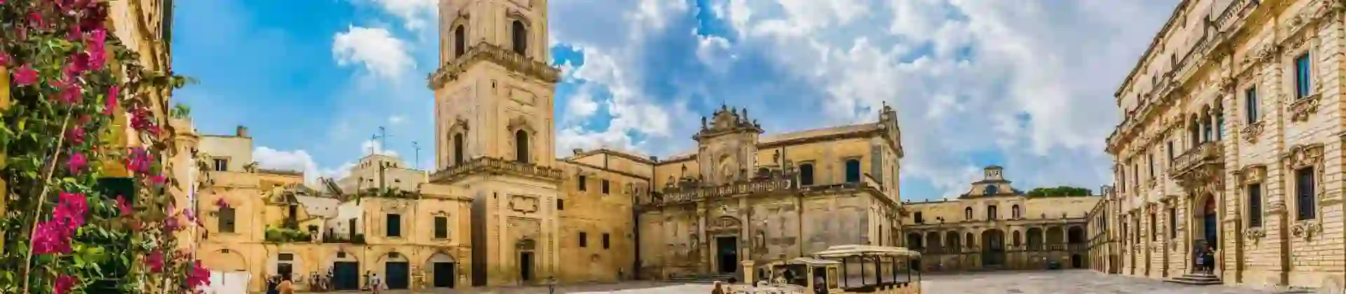 A square in Lecce, Italy, featuring a historic tower and a land train for tourists