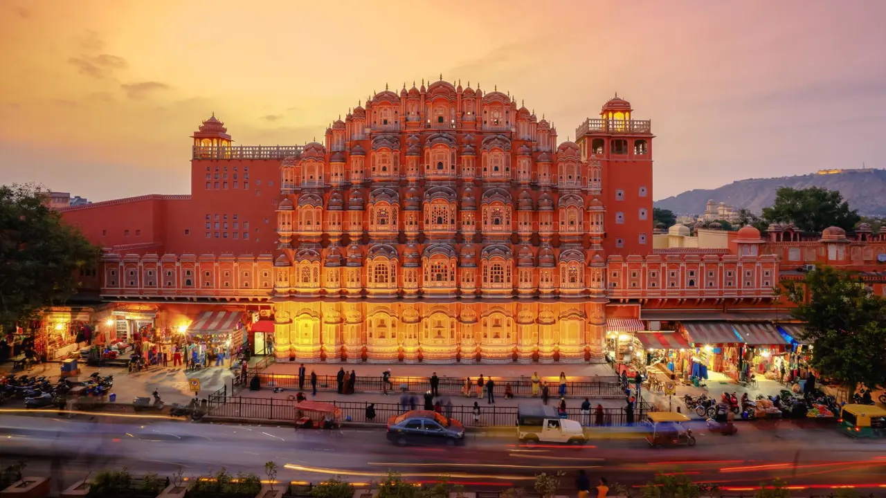 The Palace of the Winds in Jaipur illuminated at sunset, its ornate pink façade overlooking the street below