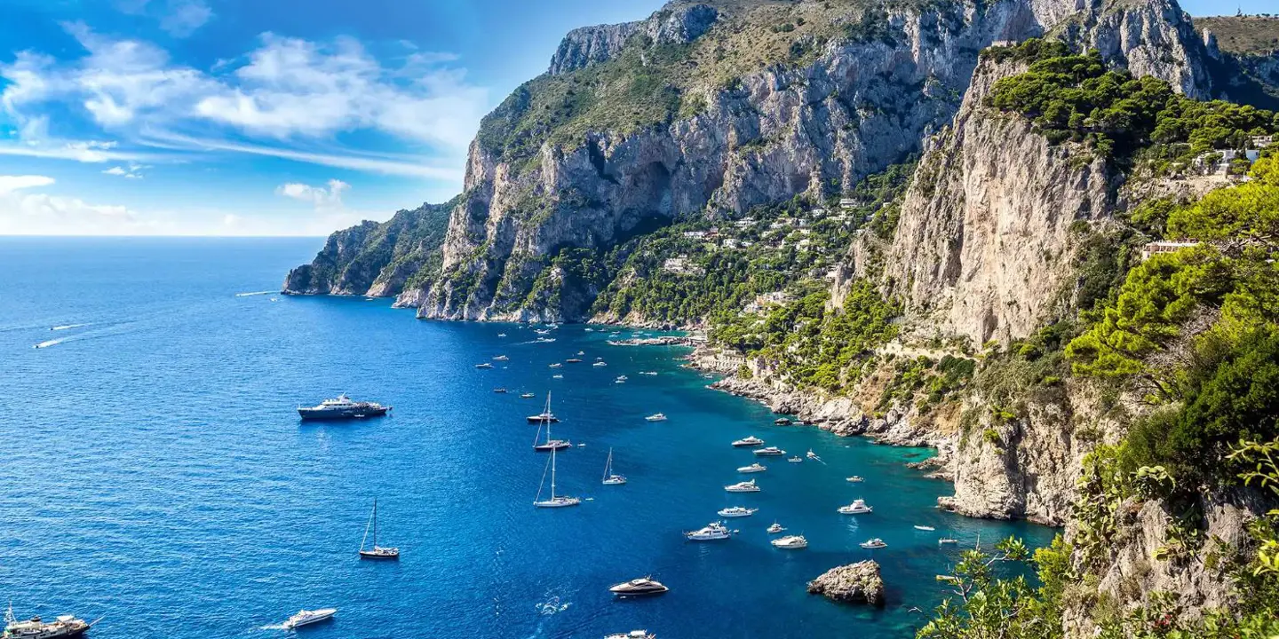 Speedboats and small yachts anchored in the turquoise waters beside Capri’s tree-covered cliffs