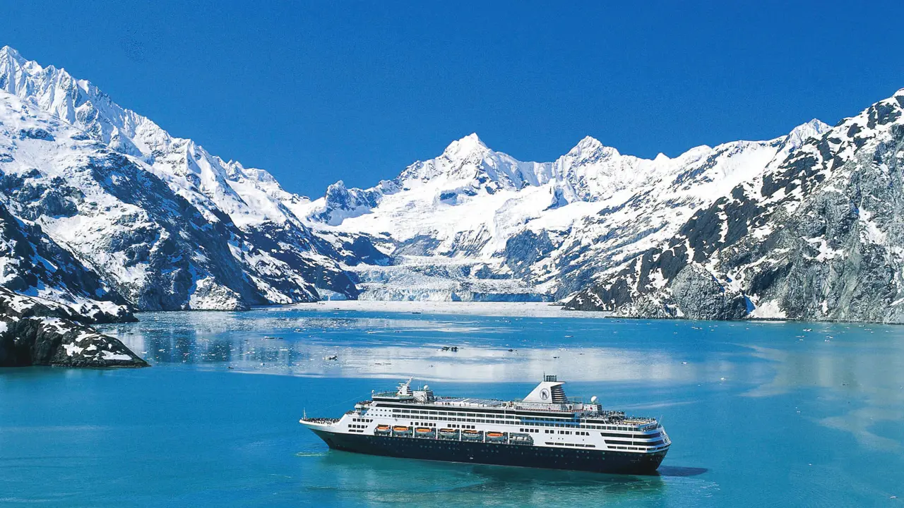 The MS Koningsdam cruise ship sailing through Glacier Bay, surrounded by calm icy waters and dramatic snow-capped mountains