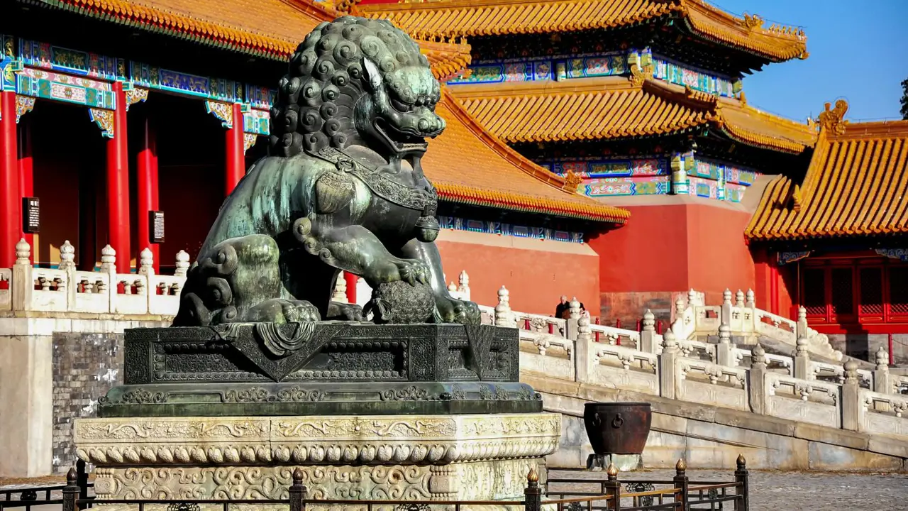 Detailed bronze lion statue before red and gold palace structures in the Forbidden City, Beijing, China