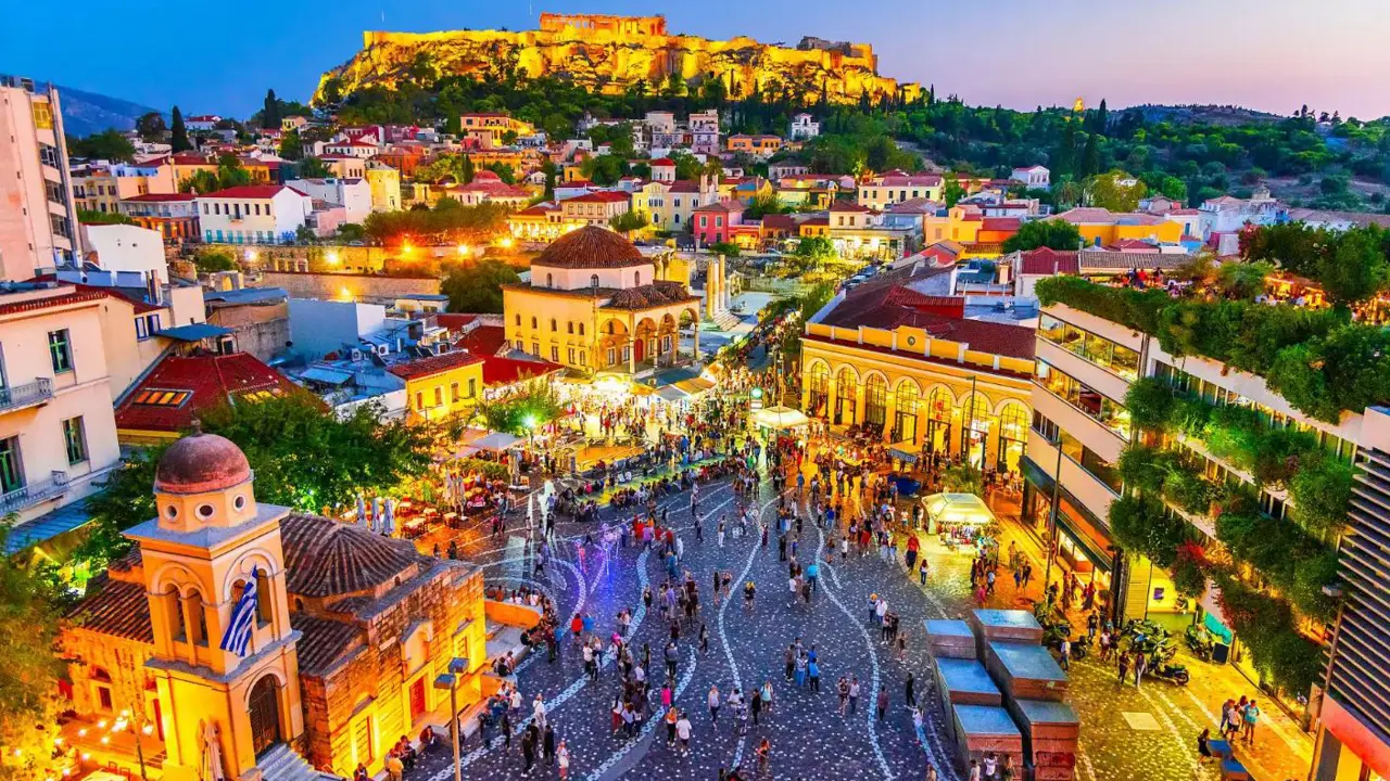 Vibrant evening scene in Monastiraki Square in Athens, with the Acropolis illuminated in the background