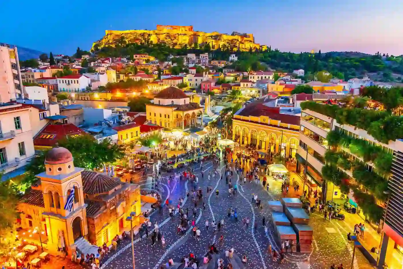 Vibrant evening scene in Monastiraki Square in Athens, with the Acropolis illuminated in the background