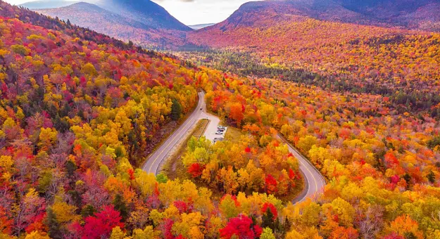 Kancamagus Highway in New Hampshire lined with vibrant autumn foliage, featuring a winding road surrounded by trees in shades of red, orange, and yellow