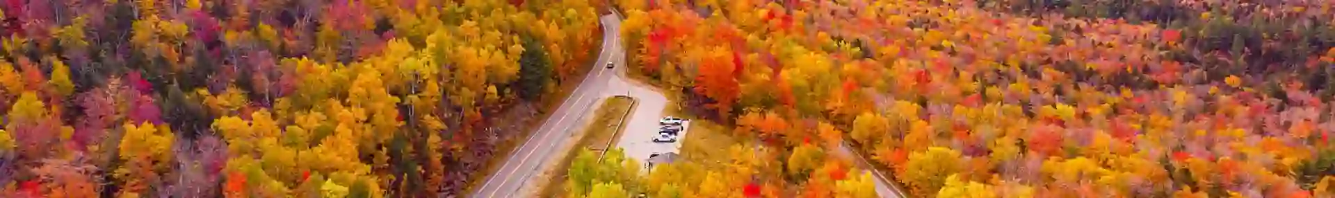 Kancamagus Highway in New Hampshire lined with vibrant autumn foliage, featuring a winding road surrounded by trees in shades of red, orange, and yellow