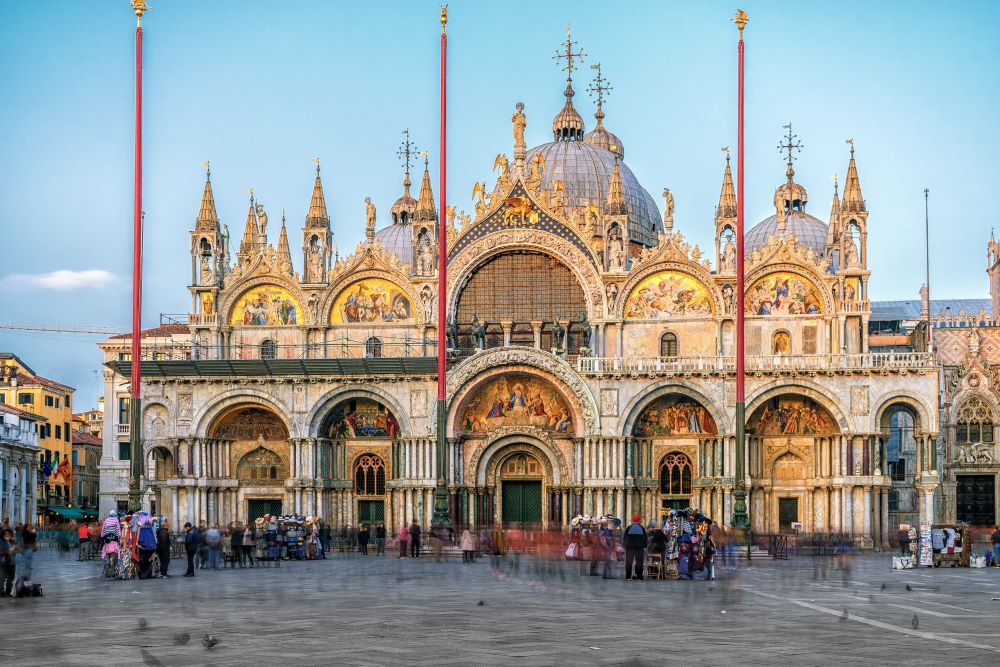 Exterior view of Saint Mark’s Basilica in Venice, Italy, showcasing its ornate façade with domes, arched windows, and detailed mosaics, reflecting Byzantine architectural style