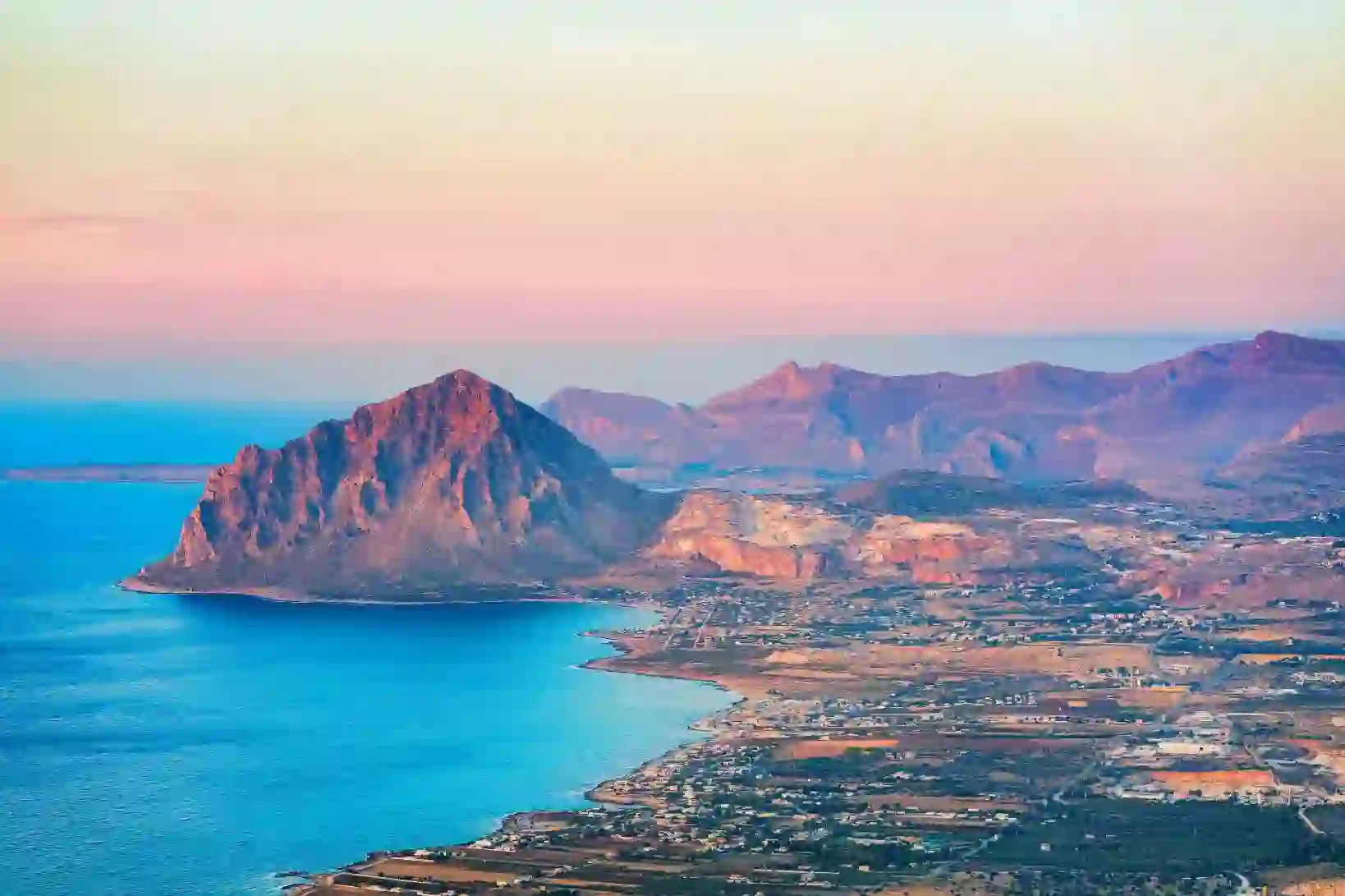 Mountain landscape of Erice, Sicily, showing a rugged hill with green vegetation and buildings clustered near the coastline below