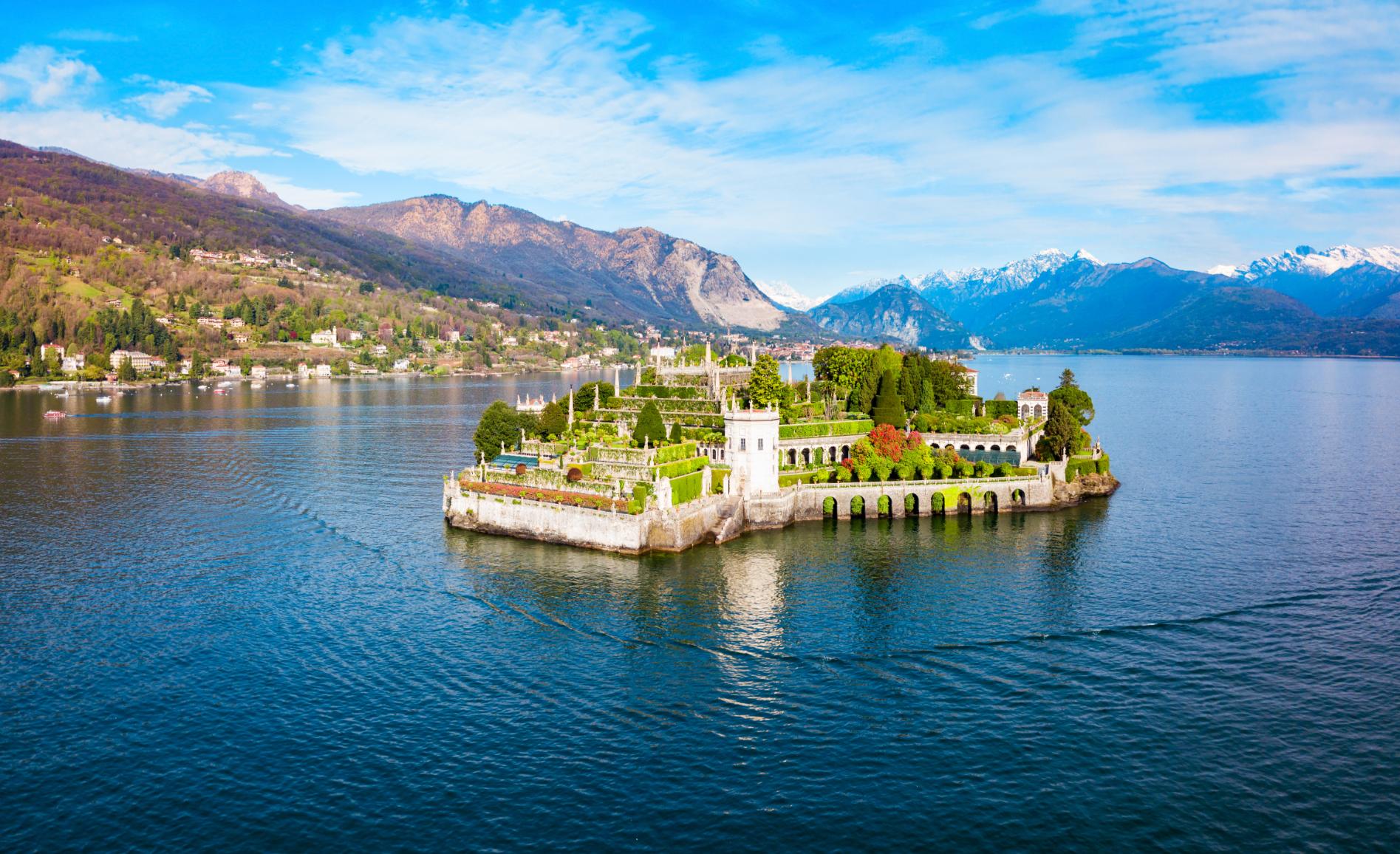 A picturesque view of Isola Bella on Lake Maggiore in Italy, featuring its ornate terraced gardens, elegant architecture and the surrounding mountains reflected in the water