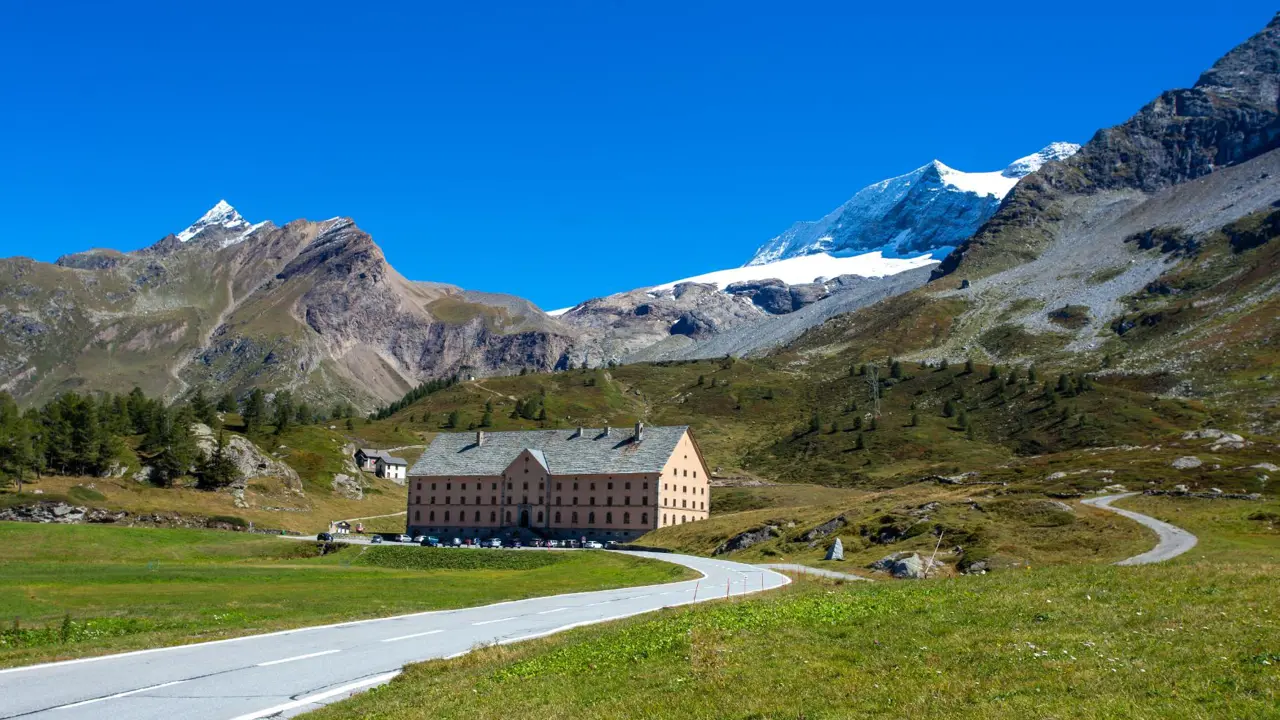 Simplon Pass in Switzerland, featuring the historic Simplon Hospice at the centre, surrounded by snow-covered alpine peaks and rugged mountain scenery