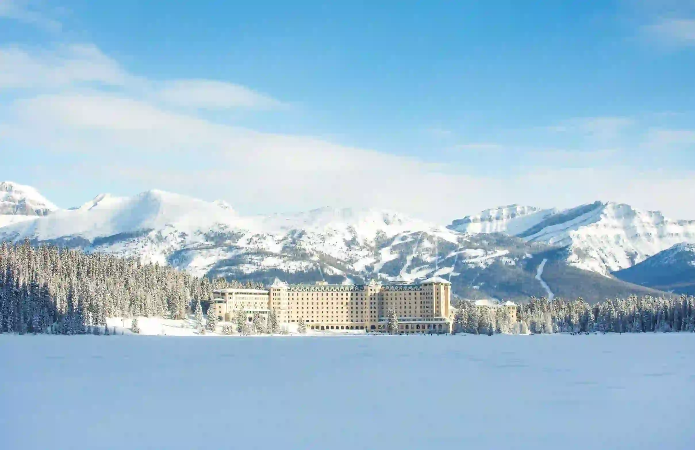 Fairmont Chateau, Lake Louise surrounded by snow-covered trees and mountains under a clear blue sky in winter