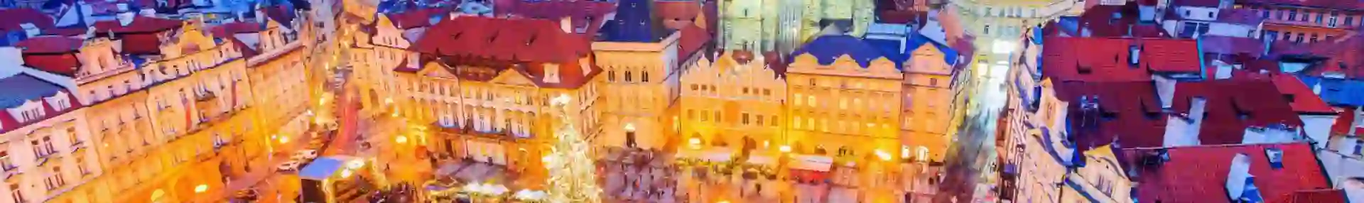 High angle shot of a Christmas market in the town square of Prague, showing a lit up gothic church with two towers and a large lit up Christmas tree