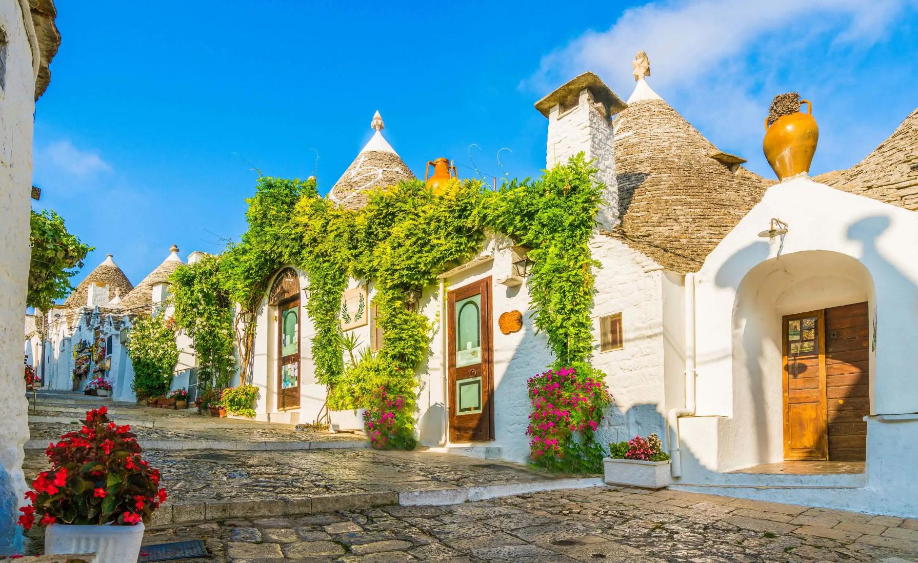 View of traditional white Trulli houses with conical stone roofs in Alberobello, Apulia, Italy, under a clear blue sky