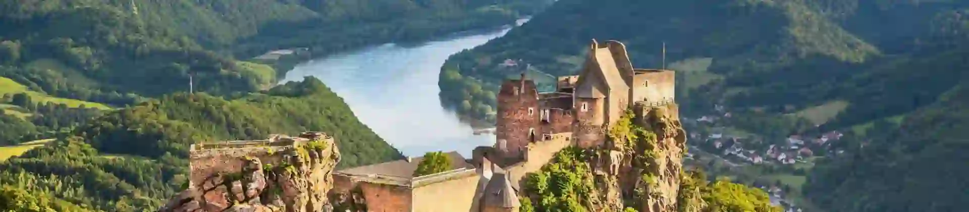 Ruins of a medieval castle perched on a rocky hilltop overlooking the Danube River in the Wachau Valley, Austria, surrounded by lush green hills and distant mountains