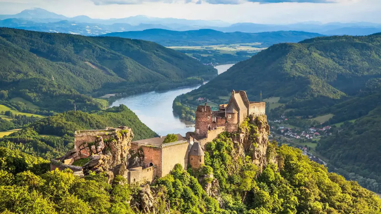 Ruins of a medieval castle perched on a rocky hilltop overlooking the Danube River in the Wachau Valley, Austria, surrounded by lush green hills and distant mountains