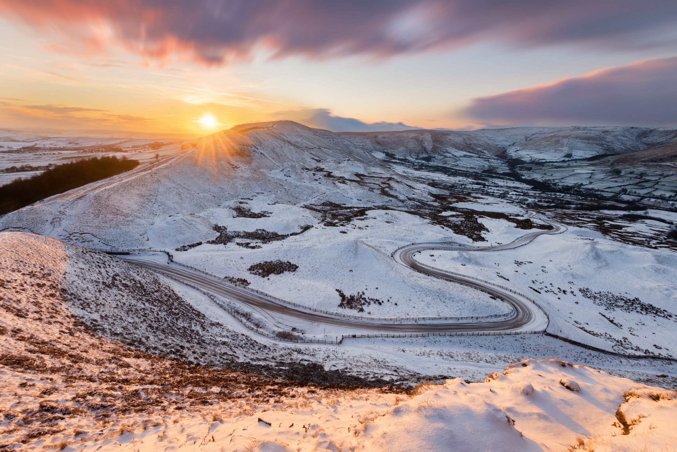 View of the Peak District at winter, with snowy mountains and the sun creeping over the edge of the land